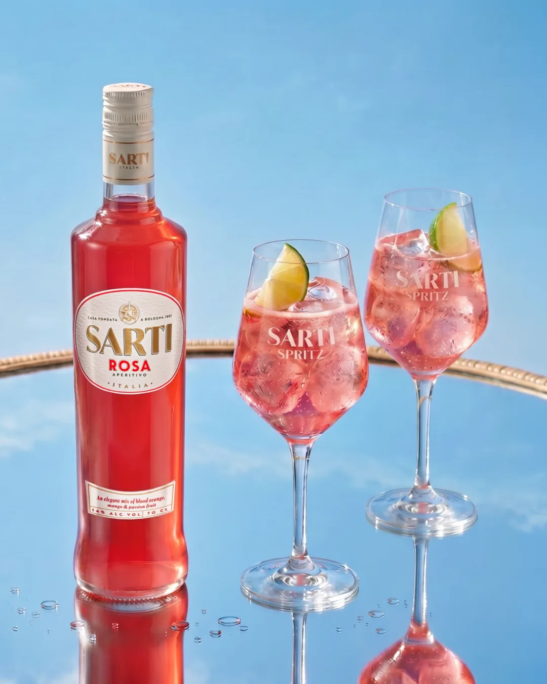Una bottiglia di Sarti Rosa accanto a due calici di Sarti Spritz con ghiaccio e una fetta di lime